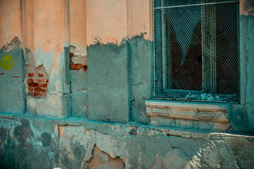 Orange old building with very weathered plaster with a wooden framed broken window with rusty metallic grid over it – Weak construction in ruins with a damaged facade