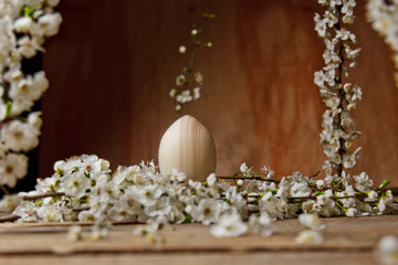 wooden easter eggs among flowering cherry branches on a rustic table. symbolic composition of the spring holiday for a gift card. copy space. close up. petals of white flowers. the rebirth of nature