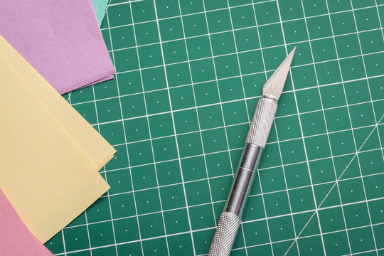 Sharp knife for cutting paper on cutting mat near coloured papers for origami