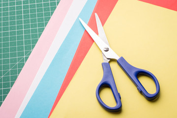 Blue scissors on papers of different colour for making origami