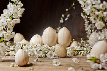 Obraz na płótnie Canvas wooden easter eggs among flowering cherry branches on a rustic table. symbolic composition of the spring holiday for a gift card. copy space. close up. petals of white flowers. the rebirth of nature