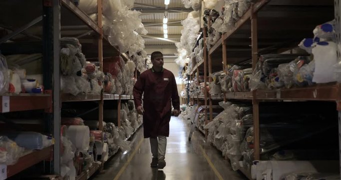 In slow-motion shooting, a guy (man) at a factory (in a warehouse) chooses different rolls of cloth worn in a work coat. Concept of: Work, Warehouse, Consumer, Handyman, Quality Assurance.