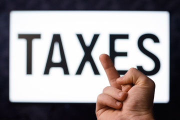 Taxes reform. Frustrated man showing middle finger to a screen with inscription TAXES