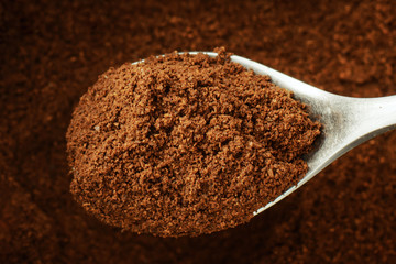 Coffee powder on spoon against a background of ground coffee