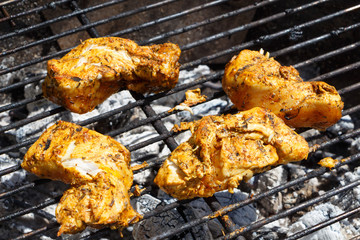 Marinated chicken pieces grilling on the grid of a barbecue