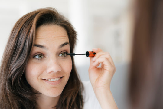 Pretty woman applying make up, using mascara