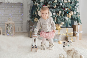 Beautiful girl near decorated Christmas tree with toy wooden rocking horse