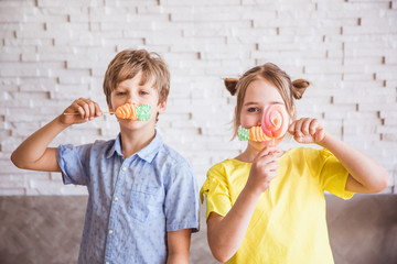 Adorable girl and boy holding colorful sweet meringues on a stick on Easter day