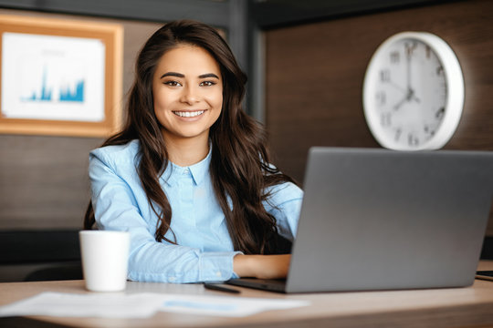 Photo of beautiful young manager woman with bright smile working with laptop in modern office.
