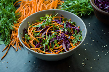 Salad of red cabbage, carrots and greens. Decorated with sliced vegetables and herbs. Cutting strips. Dark background.