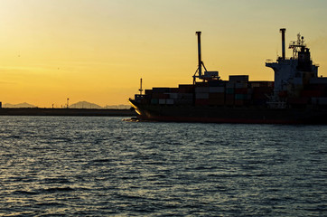 夕焼けの港を出る貨物船
