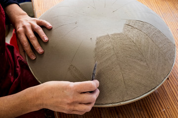 High angle close up of ceramic artist working on clay bowl, applying pattern with hand tool.