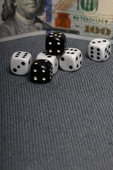 White dice with black markings. They lie on a surface covered with a coarse gray cloth. Among them are two black dice with white markings. Nearby is a hundred dollar bill.