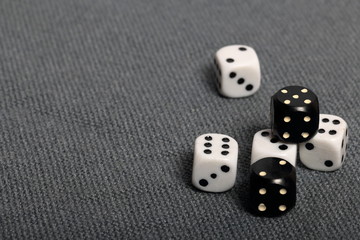 White dice with black markings. They lie on a surface covered with a coarse gray cloth. Among them are two black dice with white markings.