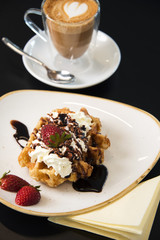 Cafe tabletop with sweet pastries, strawberries and cream and coffee latte. 