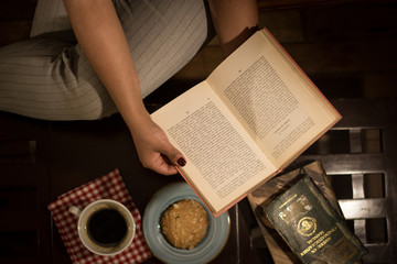 mujer leyendo un libro sobre una mesa con café y galleta