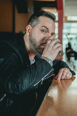 Man in a bar at the counter looks up at the camera with raised eyebrow and whiskey in his hand