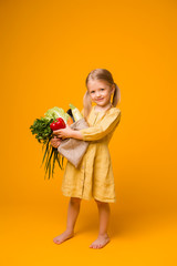baby girl with eco bag and vegetables. baby girl blonde holding eco bag with vegetables on yellow background isolate, space for text, concept organic food