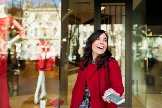 Happy woman holding cell phone in front of shop window