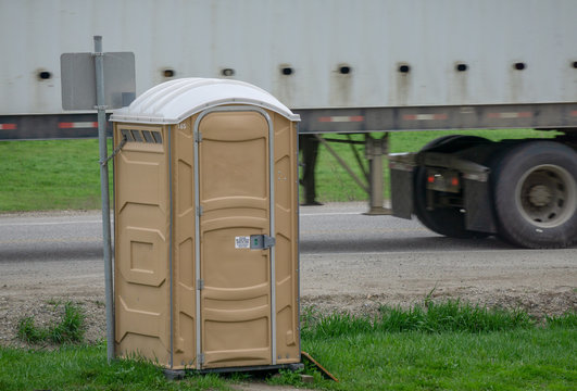 Portapotty on a roadside with truck passing