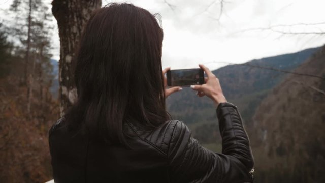 Young woman makes photo of mountain river landscape on smartphone camera, to share on internet social media through photo application for mobile device.