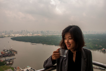 Fototapeta na wymiar The girl standing drinking coffee on the balcony of the condominium looked at the river.