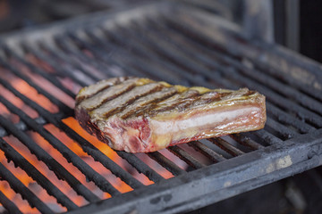 A large steak on the bone is prepared on the barbecue grill restaurant kitchen