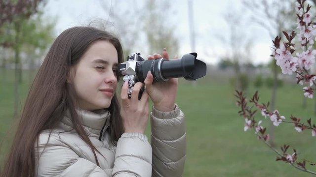A girl is taking pictures of flowers. Young girl photographer in a blooming garden.