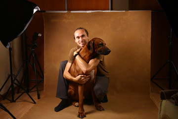 Fototapeta na wymiar Studio shot of a man with Rhodesian Ridgeback Dog on brown Background