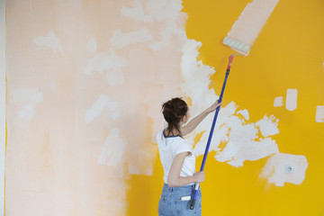 Woman painting with white paint over a yellow wall 