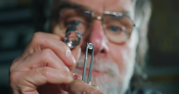 Slow motion close up of experienced goldsmith controlling a quality of diamond stone, selected for making jewels in workshop. Shot in 8K. Concept of jewelry,luxury,goldsmith, diamonds, brilliance