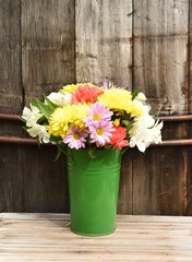 Spring flower bouquet in green metal bucket vase against rustic background