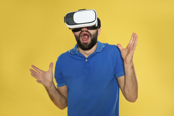 Naklejka premium Emotional young man playing video games with virtual reality headset on color background