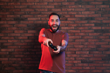 Emotional man playing video games with controller near brick wall © New Africa