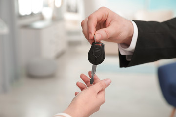 Man giving car key to woman indoors, closeup. Space for text