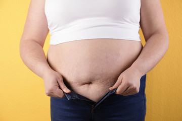 Overweight woman trying to wear tight jeans on color background, closeup