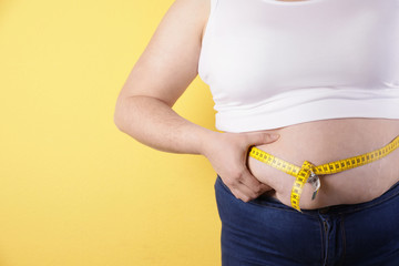 Overweight woman measuring waist with tape on color background, closeup. Space for text