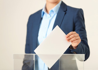 Woman putting vote into ballot box against light background, closeup