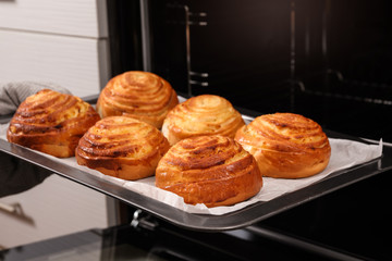 Woman taking freshly baked buns out of oven, closeup