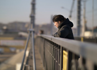 Lonely young girl stands on the bridge on a sunny day