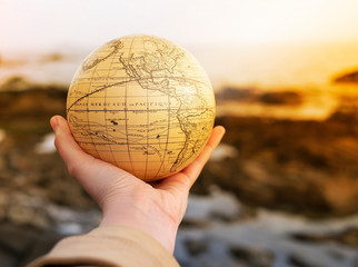 Vacation travel summer weekend sea adventure trip concept. Vintage antique globe in hand on sea and rocks background. Copy space. Mock up for turism agency. Sunset vibes. Education and discovery idea