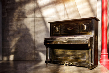 Old shabby black piano near the wall. Sunset light