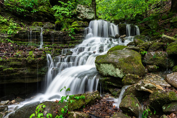 A waterfall cascades down the lush green forest of the Arkansas Ozark Mountains between Boxley Valley and Ponca.