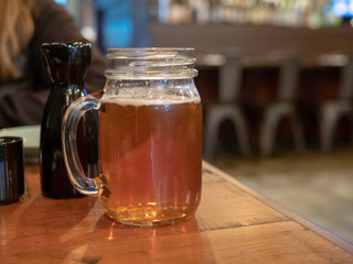 Mason jar mug with handle filled with beer next to sake bottle at restaurant - Powered by Adobe