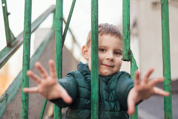 The child is behind bars. A little boy is behind a metal fence.