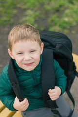 A little boy with a large backpack on the bench.