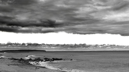A Blanket of dramatic clouds covers the sky as a storm brews along the horizon, in black & white