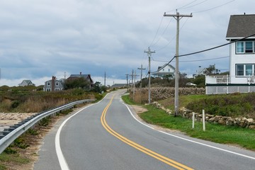 A winding road leads into the distance, among smallhouses, grass and bushes, and power line poles, Block Island, RI, USA