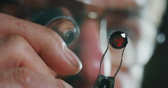 Slow motion acro close up of experienced goldsmith controlling a quality of rubin stone, selected for making jewels in workshop.Shot in 8K. Concept of jewelry,luxury,goldsmith, diamonds, brilliance.