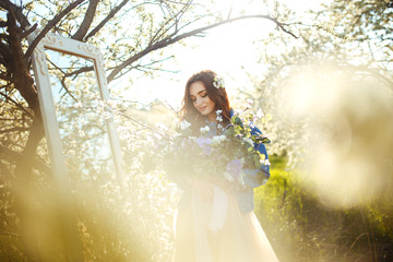Portrait of a beautiful bride. Wedding concept. Stylish wedding. Great sunset light. She is wearing a blue denim jacket, dress. Spring blooming garden.